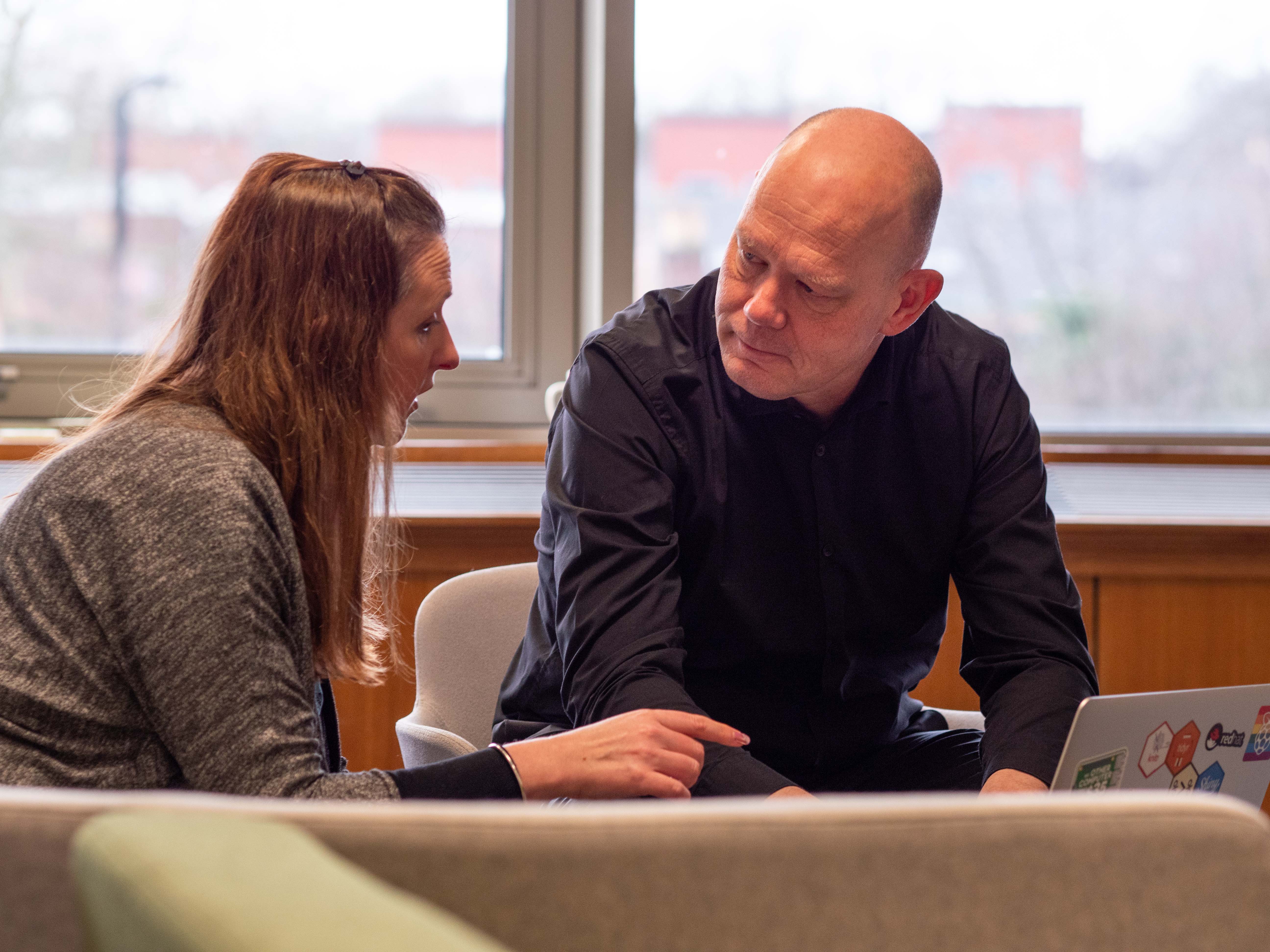 Pieter, wearing a black shirt, sitting in an informal meeting area, talking to a female colleague