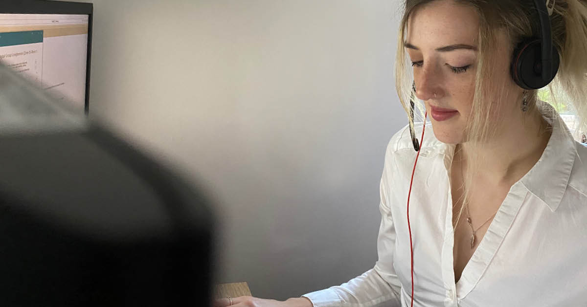 Lizy, a young woman, working on a computer, wearing a headset and a white shirt
