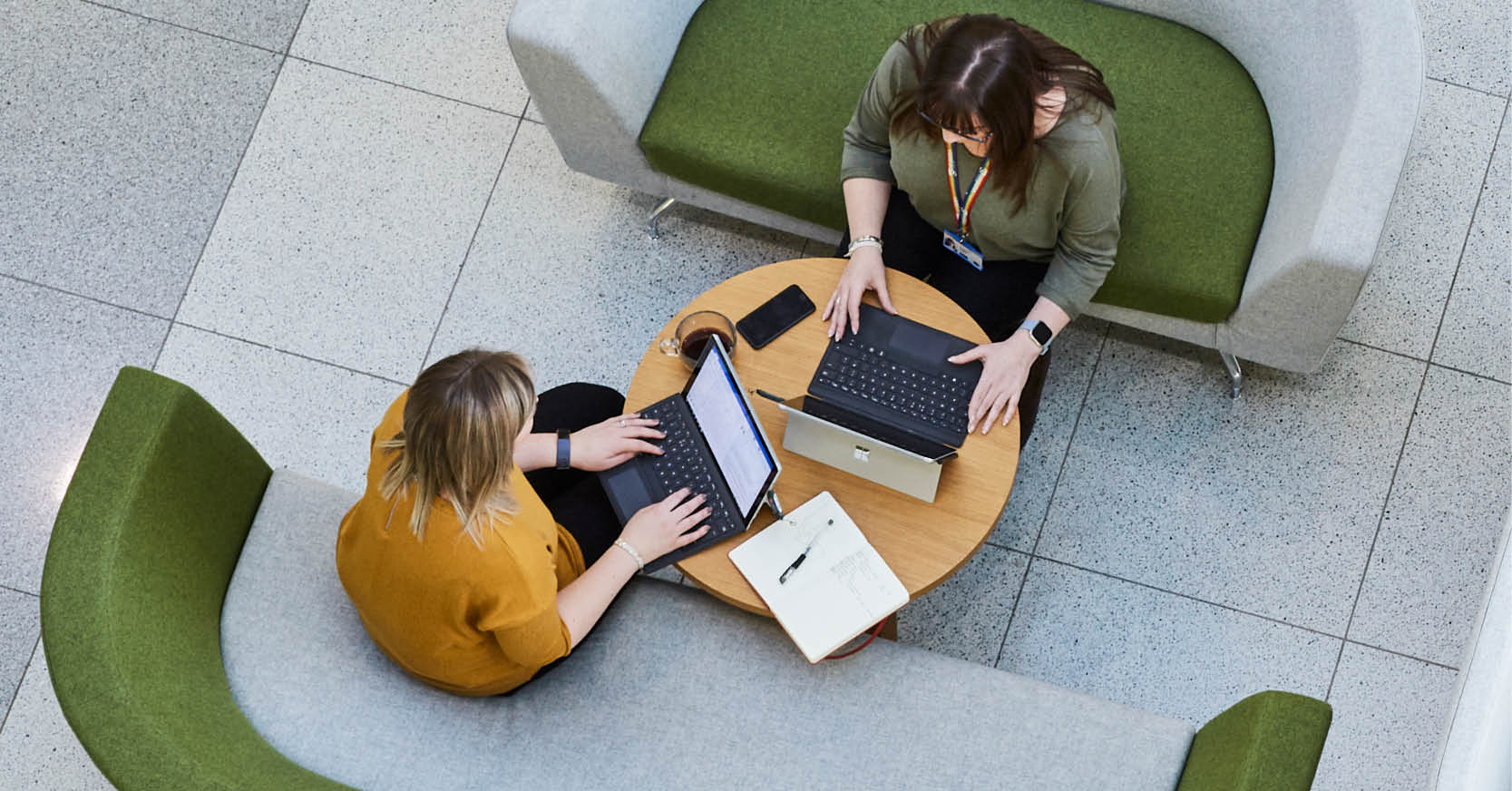 Top-down photo of two people working on laptops at an office cafeteria table