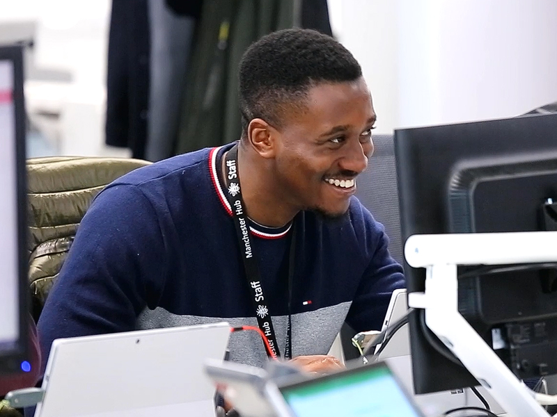 A young man sitting at a desk, leaning forward and smiling