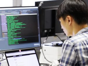 Man working on computer. There are lines of code on the screen in front of him.