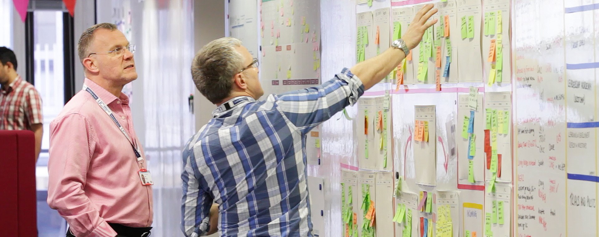 Two men looking at a whiteboard covered in paper post-it notes