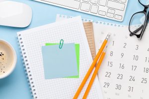 Top-down view of notebooks, pencils, a calendar and a coffee cup on a desk