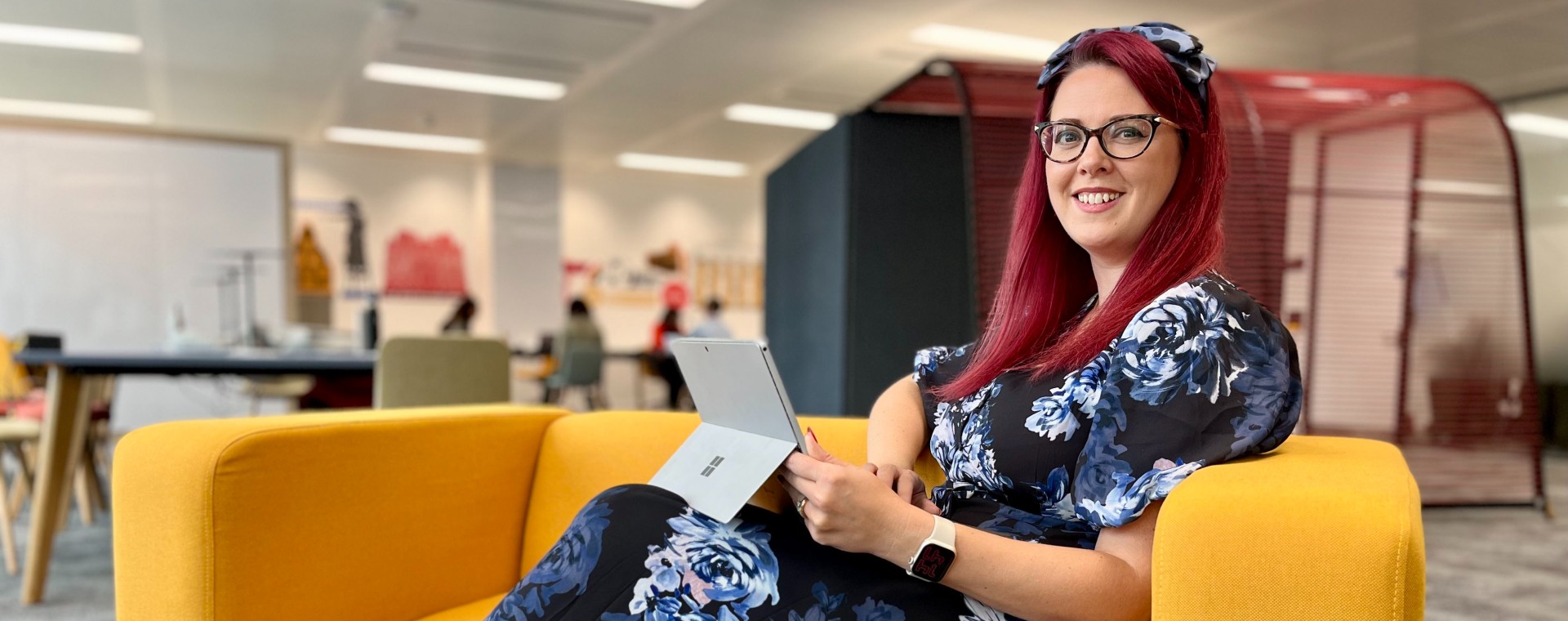 Happy woman sat in an open plan office at DWP Digital.