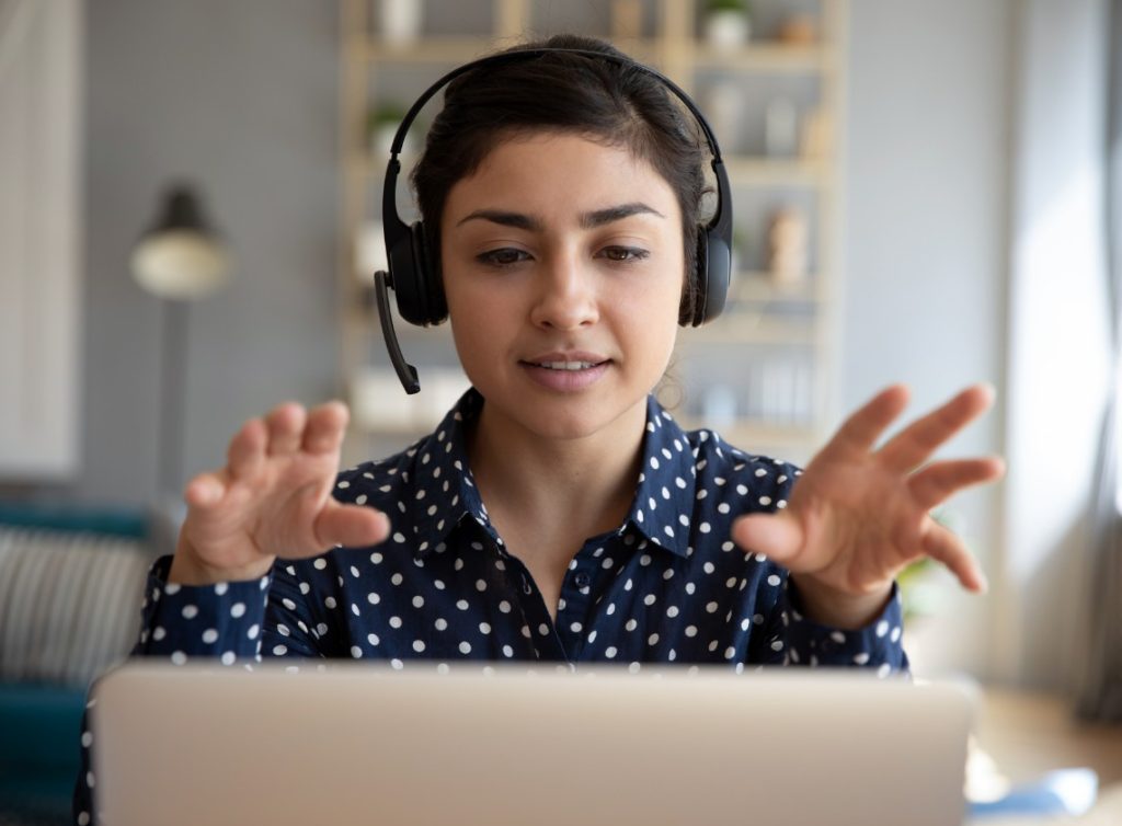 A woman wearing a headset gestures with her hands as she speaks on a video call