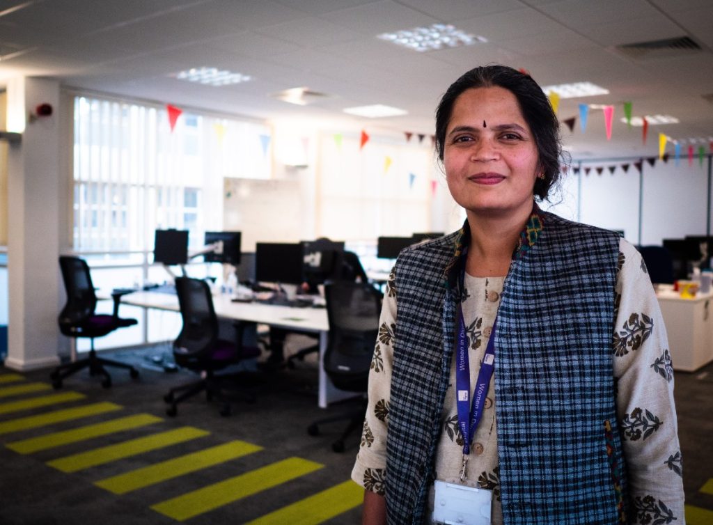 Technical architect Rashmi stands in an open plan office.