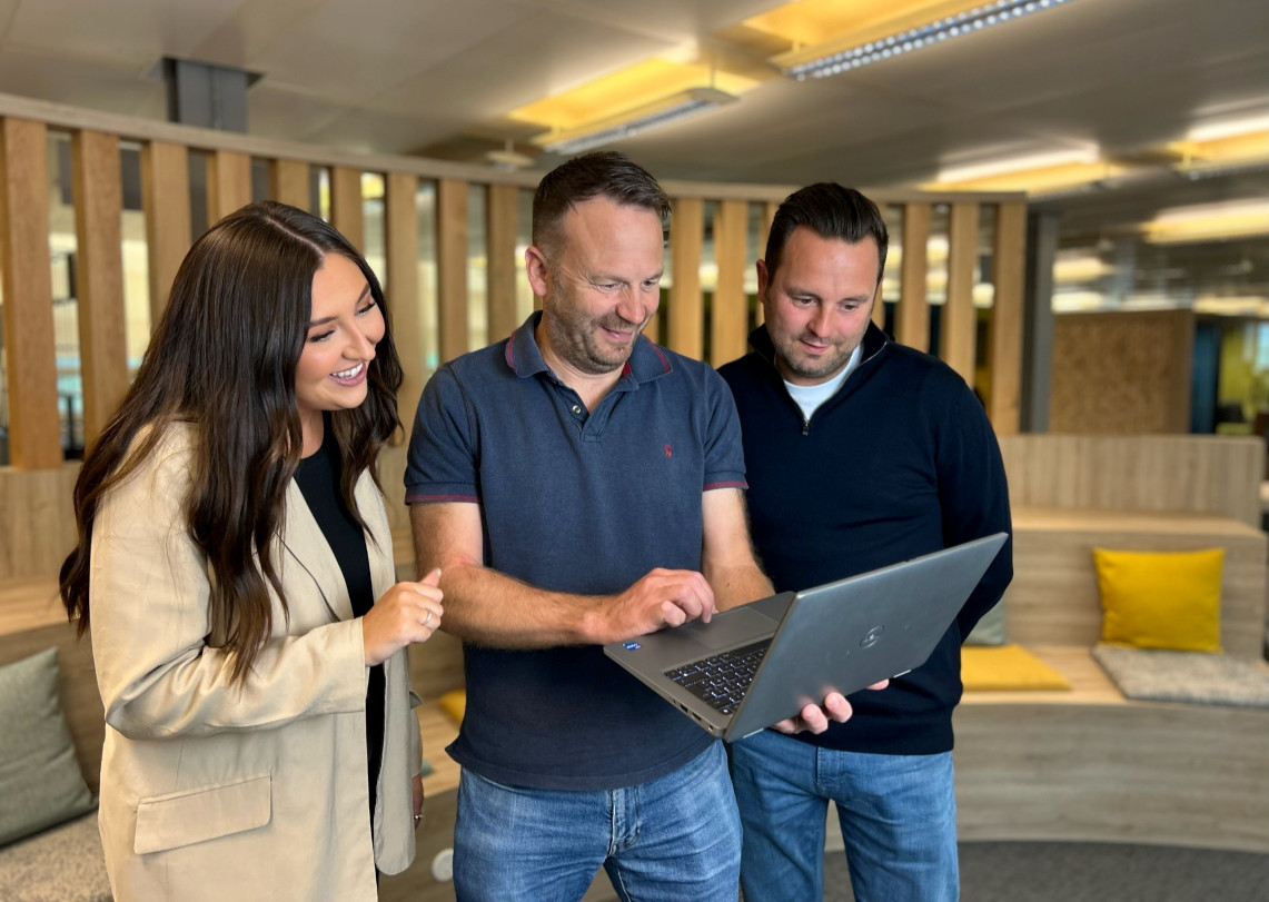 Three colleagues looking at a laptop in a DWP open plan office.