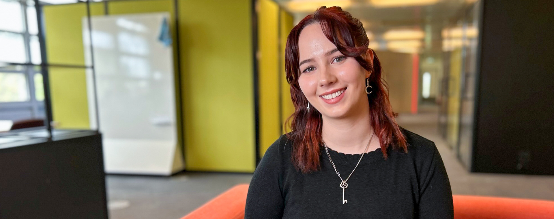 A young woman sat in a DWP office, smiling.