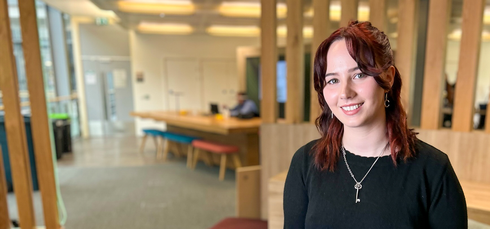 Young woman in a black top smiling at camera in an open office setting.