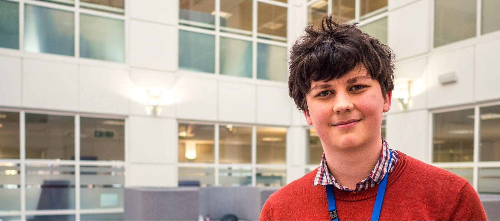 Young man in bright sweater smiling at camera in office reception.