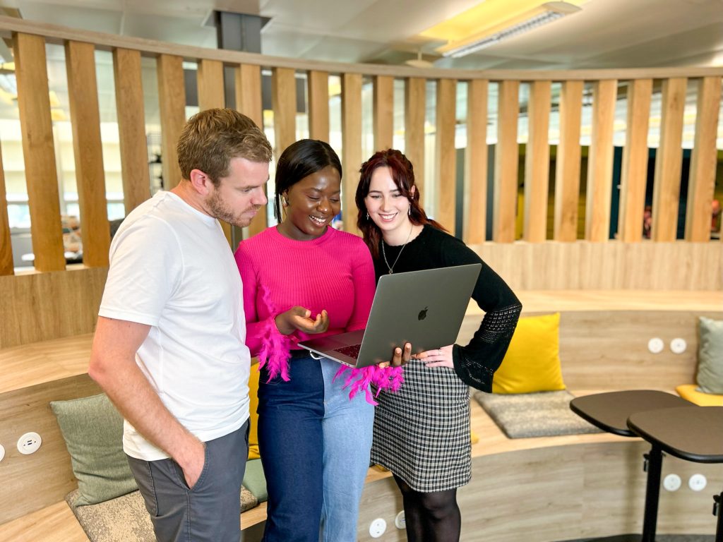 Three colleagues looking at a laptop, looking happy.