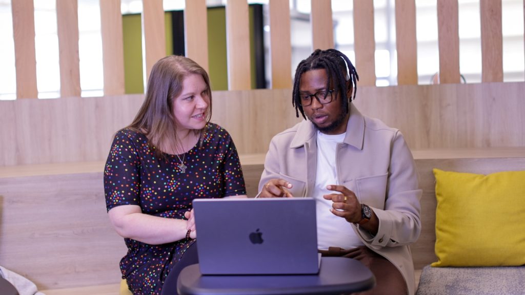 A female and male colleague talking to eachother whilst looking at a laptop.