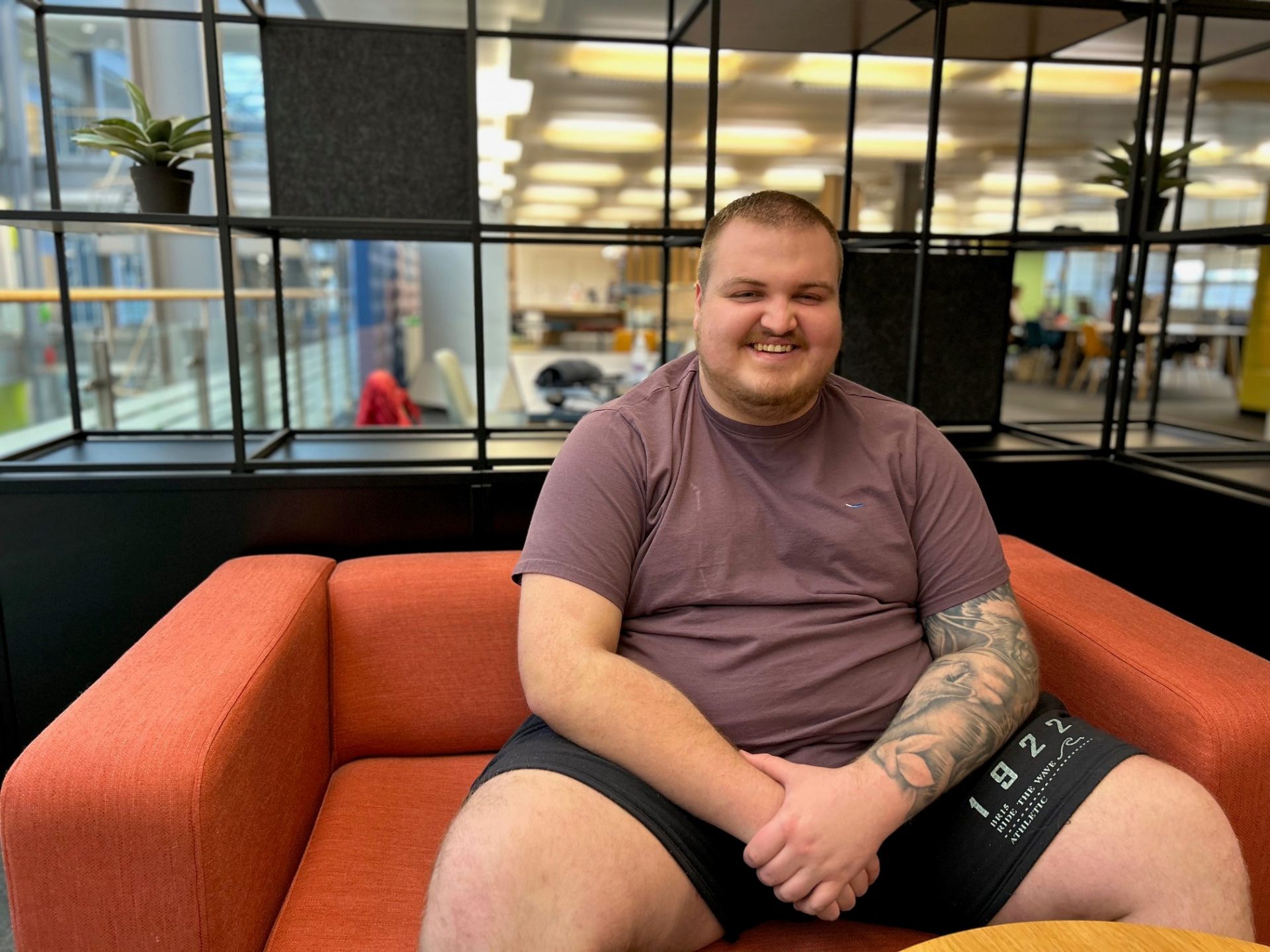 Man smiling to camera and sat on an orange sofa.