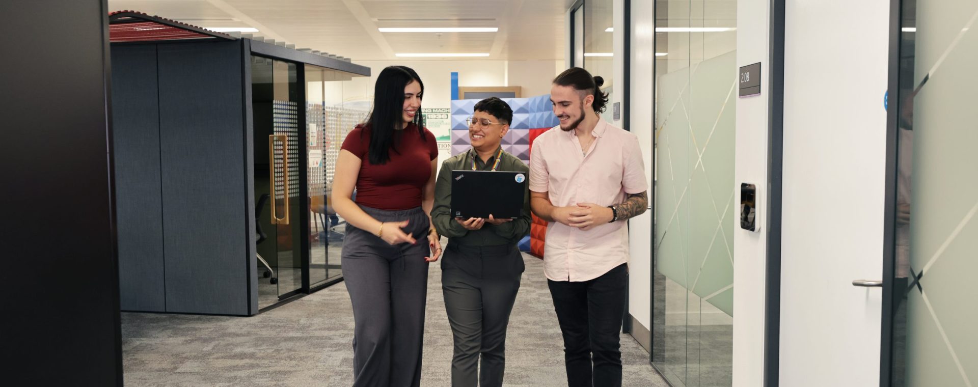 Three people walking through an office environment and smiling at one another.